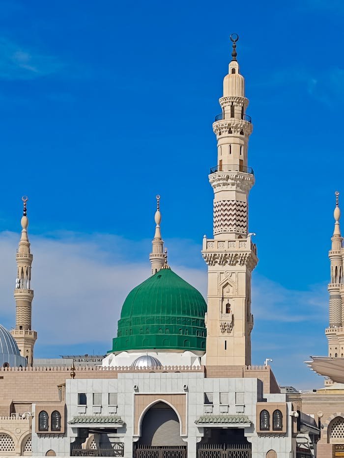 A clear and detailed view of the minarets and green dome of Al-Masjid an-Nabawi against a bright blue sky.