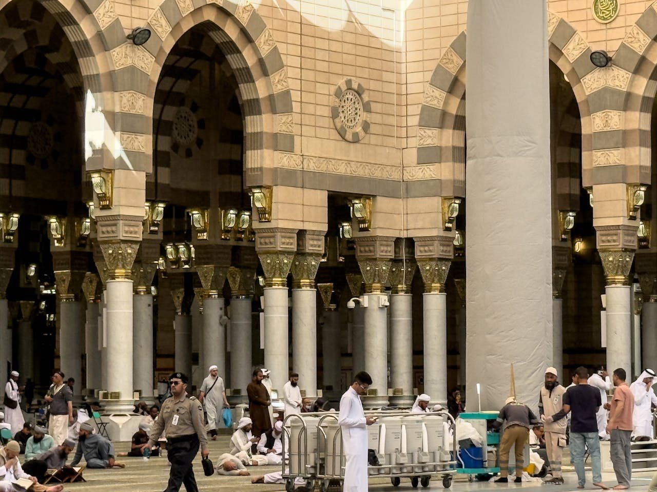 A bustling scene inside Al-Masjid an-Nabawi in Medina, featuring people and intricate architecture.